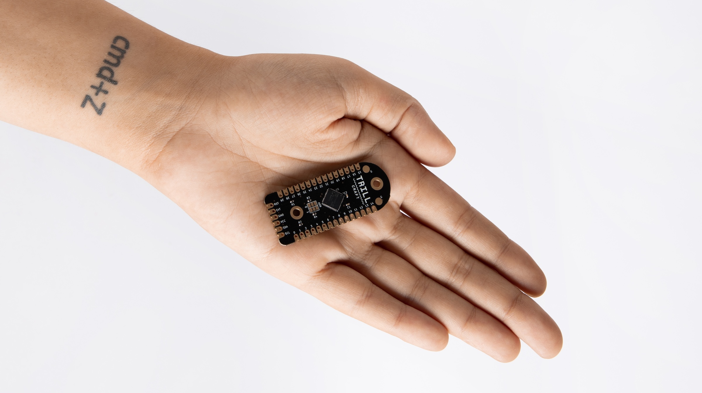 A Trill Bar sensor held in a hand against a soft-focus studio background